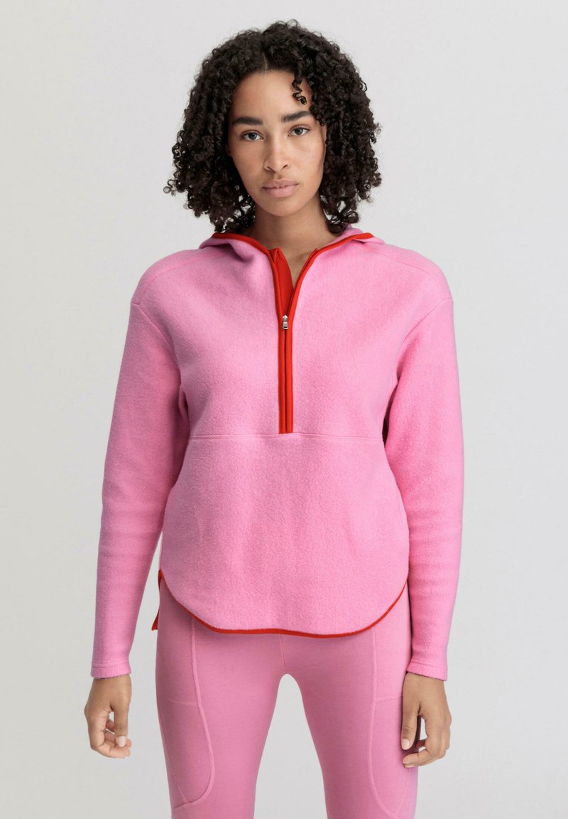 Pullover in pile rosa con colletto zip rosso e cappuccio. Presenta maniche lunghe e orlo inferiore arrotondato. Tessuto testurizzato.