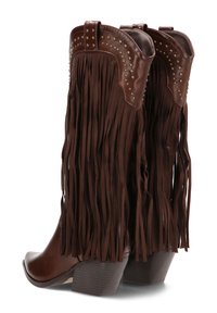 Botas de vaquero de cuero marrón con largas borlas, detalles de tachuelas en el tobillo, punta afilada y tacón grueso. Superficie texturizada en toda la bota.