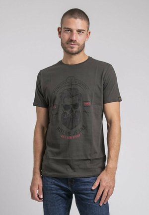 T-shirt en coton vert foncé avec un design graphique d'un crâne avec une barbe et des lunettes de soleil, texte noir et rouge, col rond, manches courtes.