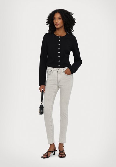 Czarny długi rękaw top z okrągłym dekoltem i srebrnymi guzikami, w połączeniu z jasnoszarymi rurkami i czarnymi sandałami na obcasie z paskami.