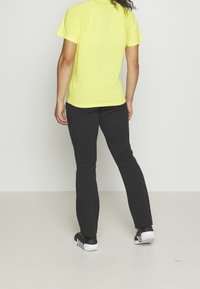 Kurzärmliges, leuchtend gelbes Sportshirt mit strukturierter Oberfläche, kombiniert mit schwarzen, enganliegenden Hosen und schwarzen Sportschuhen mit weißen Akzenten.