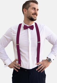 Burgunderfarbene Hosenträger und eine Fliege, kombiniert mit einem weißen Hemd. Das Hemd hat eine Knopfleiste vorne und Manschettenknöpfe. Dunkle Hosen runden den Look ab.