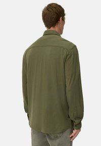 Oliwkowa koszula z długim rękawem o teksturowanym wykończeniu, z guzikami przy mankietach i prostym szwem na plecach. Sylwetka w fasonie slim fit.