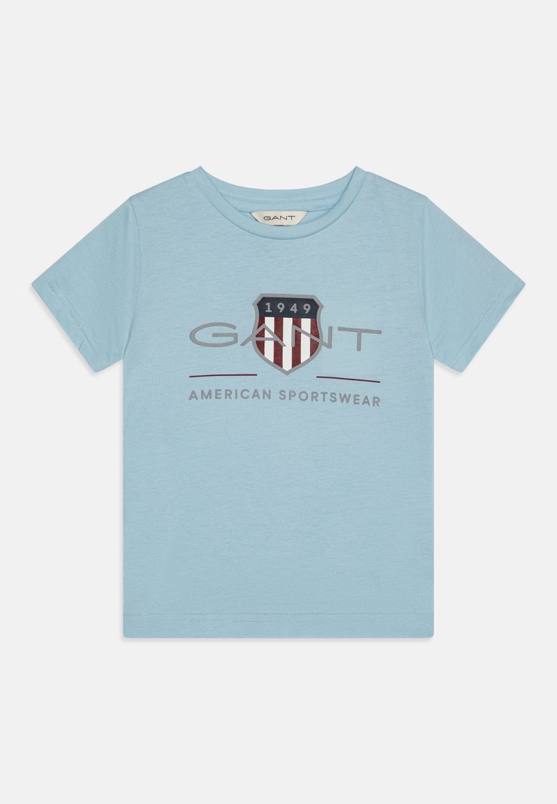 Camiseta de algodón azul claro con mangas cortas, que presenta un logo en forma de escudo en navy y rojo y el texto "GANT AMERICAN SPORTSWEAR" en el centro.
