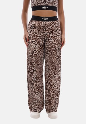 Donna che indossa pantaloni larghi con stampa leopardata e crop top abbinato con fasce nere in vita con la scritta "Gaelle Paris", in piedi con le mani ai lati.