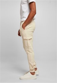 Beige cargo joggers featuring a fitted design, side pockets, and cuffed ankles, paired with white sneakers against a neutral background.