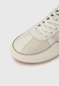 Χαμηλών σπορ παπουτσιών σε εκρού δέρμα και σουέτ με ραμμένο σχέδιο, υφασμένα διακοσμητικά στοιχεία και επίπεδα κορδόνια. Διαθέ τει αντίθετη σόλα από καουτσούκ.