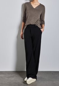 Ruskea neulottu v-kaula-aukollinen neule yhdistettynä mustiin leveälahkeisiin housuihin, joissa on vyölenkki ja nappikoriste, täydentäen asua valkoisilla lenkkareilla.