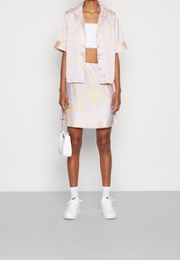 Fialové a žluté pruhované tričko s krátkým rukávem a odpovídající sukni, doplněné bílými teniskami a malou bílou kabelkou.