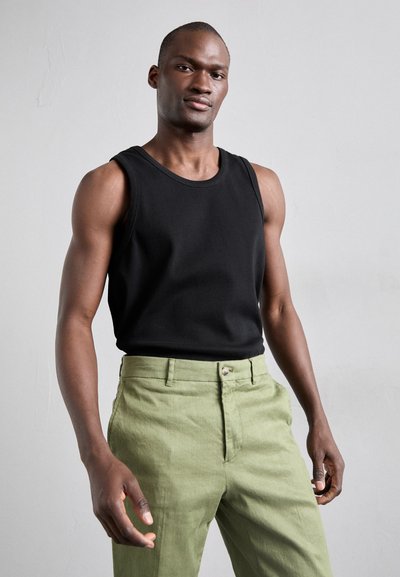 Zwarte geribbelde tanktop gecombineerd met lichtgroene, gestructureerde broek met een knoopsluiting aan de voorkant en zijzakken.