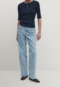 Marineblå ribbet kortærmet skjorte med knapper, parret med lyseblå vide jeans. Outfittet suppleres med sorte sko.