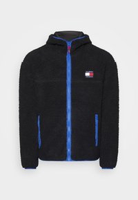 Giacca in pile nera con zip frontale, accenti blu, cappuccio e una piccola patch con logo sul petto. Tessuto morbido, due tasche laterali.