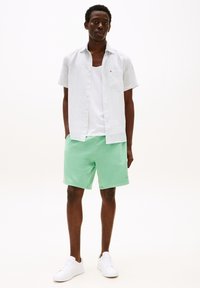 Chemise blanche à manches courtes avec de petits motifs bleus, associée à un short vert menthe et des baskets blanches. Design simple et décontracté.