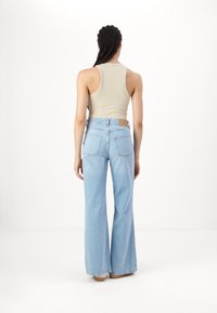 Ανοιχτού χρώματος φαρδιά τζιν με ψηλή μέση και πίσω τσέπες, σε συνδυασμό με ένα μπεζ ριγέ αμάνικο τοπ, που αναδεικνύει άνετη εφαρμογή και λεία υφή.