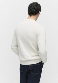 Gråvit stickad tröja med rund hals och ribbad nederkant, med en texturerad tygkvalitet och figurnära passform, bärs över mörka jeans.