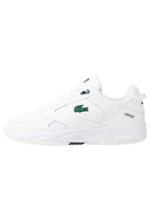 Baskets blanches de sport avec panneaux en mesh, semelle épaisse, logo crocodile vert sur le côté et fermeture à lacets.
