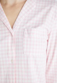 Haut de pyjama à motif vichy rose et blanc avec une poche, une fermeture à boutons et un col. Fabriqué en tissu doux, avec des coutures délicates.