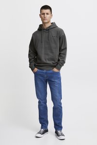 Dark grey hoodie with drawstring, featuring "A.R.C." embroidery. Paired with blue jeans and black sneakers, standing against a neutral background.