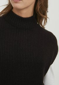 Pull en tricot noir à côtes avec un col haut. La texture du tissu est épaisse et confortable, avec une coupe décontractée et des bords nets.