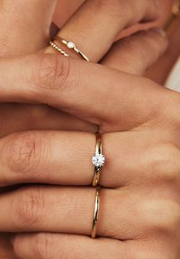 Goldringe an einer Hand: Einer hat einen runden, klaren Edelstein, während der andere ein einfacher Goldring mit strukturierter Perlenoberfläche ist.