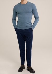 Heller blauer Strickpullover mit Rundhalsausschnitt, kombiniert mit dunkelblauen Slim-Fit-Hosen und schwarzen Slippern mit Quastenakzenten.