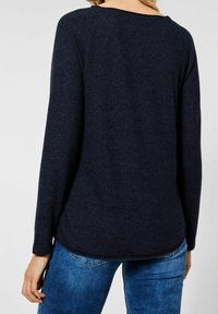 Haut à manches longues navy foncé avec un col rond, texture douce et ourlet légèrement incurvé, associé à un jean bleu.