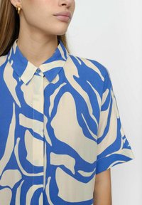 Camicia a maniche corte con bottoni, caratterizzata da un motivo astratto blu e beige, con colletto classico e un tessuto leggero e morbido.