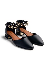 Ballerines en cuir noir avec des pointes effilées, des côtés ouverts et des accents circulaires dorés sur la sangle de cheville. Elles présentent un petit talon carré.