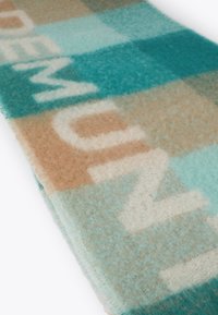 Šála z vlněné směsi s kostkovaným vzorem v barvách smaragdově zelené, světle hnědé a krémové, se slovem "PREMIUM" napsaným tučným písmem na měkké texturované tkanině.