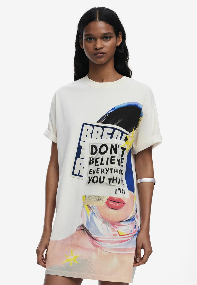 Yli suuri valkoinen t-paita, jossa on graafisia kuvastoja, mukaan lukien naisen kasvot ja teksti "ÄLÄ USKO KAIKKEA MITÄ AJATTELET", sinisin ja keltaisin korostuksin.