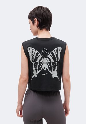 Person with short dark hair wears black sleeveless crop top featuring large white butterfly and number 72 on the back, paired with gray pants.
