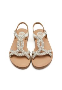 Sandalias planas beige con un diseño de tiras cruzadas, embellidas con gemas claras. Las tiras son plateadas y la plantilla es de cuero marrón claro.