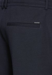 Marinblå joggingbyxor med en texturerad tyg, som har en bakficka med en svart accentband och en liten metall-logotag.