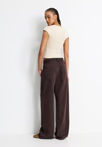 Beige enger Oberteil und lockere dunkelbraune weite Hosen mit Taschen hinten, die eine glatte Textur und einen elastischen Bund bieten.