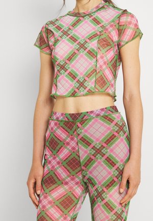 Mujer con camiseta corta y pantalones de talle alto a cuadros a juego en rosa, verde y marrón, de pie frente a un fondo liso.