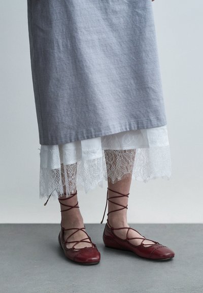 Szara lniana sukienka z białym koronkowym obszyciem i czerwone baleriny ze skóry z krzyżującymi się paskami oraz wycięciami. Płaski, zaokrąglony nosek.