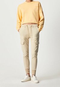 Gul kortärmad sweatshirt med bröstficka, kombinerad med beige cargojoggers med dragsko i midjan och sidofickor, bärs med vita sneakers.