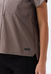 Korte mouwen bruine shirt, gemaakt van gladde stof, heeft twee borstzakken en een logo-label aan de zoom, met een relaxte pasvorm en subtiele glans.