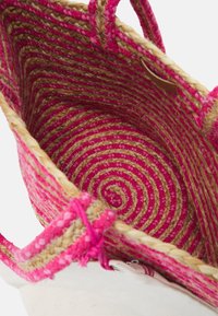 Sac fourre-tout tressé présentant un motif en spirale rose et beige, avec des anses tissées et une base en coton. L'intérieur a une texture lisse et une forme ronde.