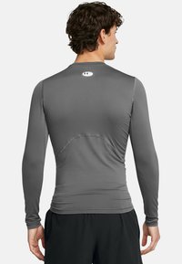 Langärmliges Kompressionsshirt in Dunkelgrau mit rundem Logo am Hals, glatter Textur und figurnahem Design, kombiniert mit schwarzen Shorts.