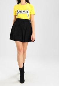 Gul bomullströja med "GRL PWR" grafik och en svart, utsvängd kjol. Outfitten är kombinerad med svarta ankelboots. Enkelt och avslappnat design.