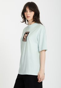 Himmelblaues Baumwoll-T-Shirt mit kurzen Ärmeln, mit einem zentralen grafischen Design in einem rechteckigen Rahmen. Einfacher, lässiger Schnitt.