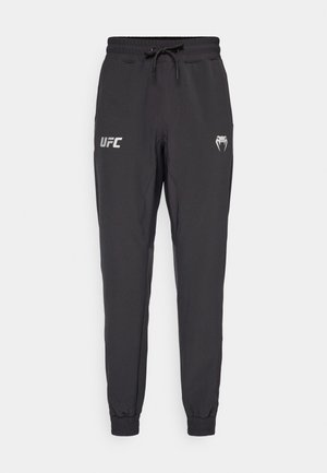 Črne športne hlače z elastičnim pasom in vrvico, ki vsebujejo UFC logo in simbol kobre, z manšeto na gležnjih ter gladko teksturo tkanine.