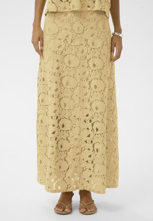 Kollakas-beezililleline maksiseelik lillemustriga, kantud sobiva topi ja beežide sandaalidega, jalad ja käed valgel taustal.