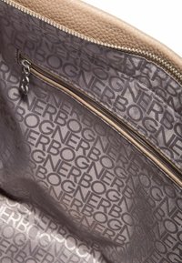 Intérieur de sac à main en cuir crème avec une texture lisse. Comprend une poche zippée et une doublure à motifs avec le logo de la marque répété.