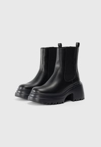 Bottines noires avec une tige en cuir texturé, des panneaux latéraux élastiques, un talon épais évasé et une semelle crantée robuste.