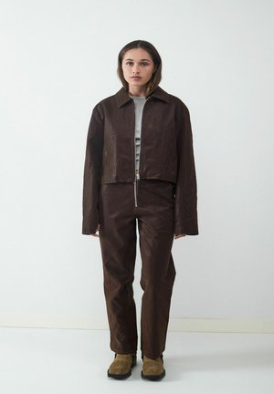 Bruine cropped jas en bijpassende broek gemaakt van glanzend textuurmateriaal, met een ritssluiting aan de voorkant, lange mouwen en een minimalistisch ontwerp.