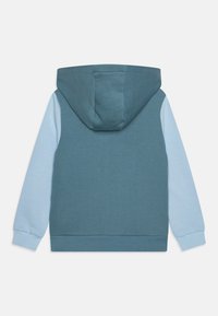 Sweat-shirt à capuche avec un corps teal et des manches bleu clair. Fabriqué en tissu doux, il possède une poche kangourou et des poignets côtelés.