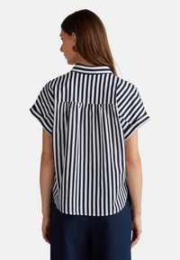 Camicia a maniche corte a righe blu navy e bianche con colletto, dotata di dettagli arricciati sul retro e orlo curvo. Tessuto dalla consistenza liscia.