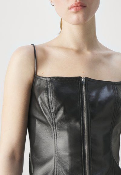Haut en cuir noir avec décolleté carré, bretelles fines et fermeture éclair centrale, mettant en avant une texture lisse avec des détails de couture subtils.